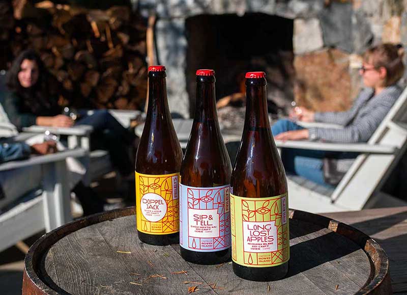 Riley's Cidery bottles on barrels in front of fireplace